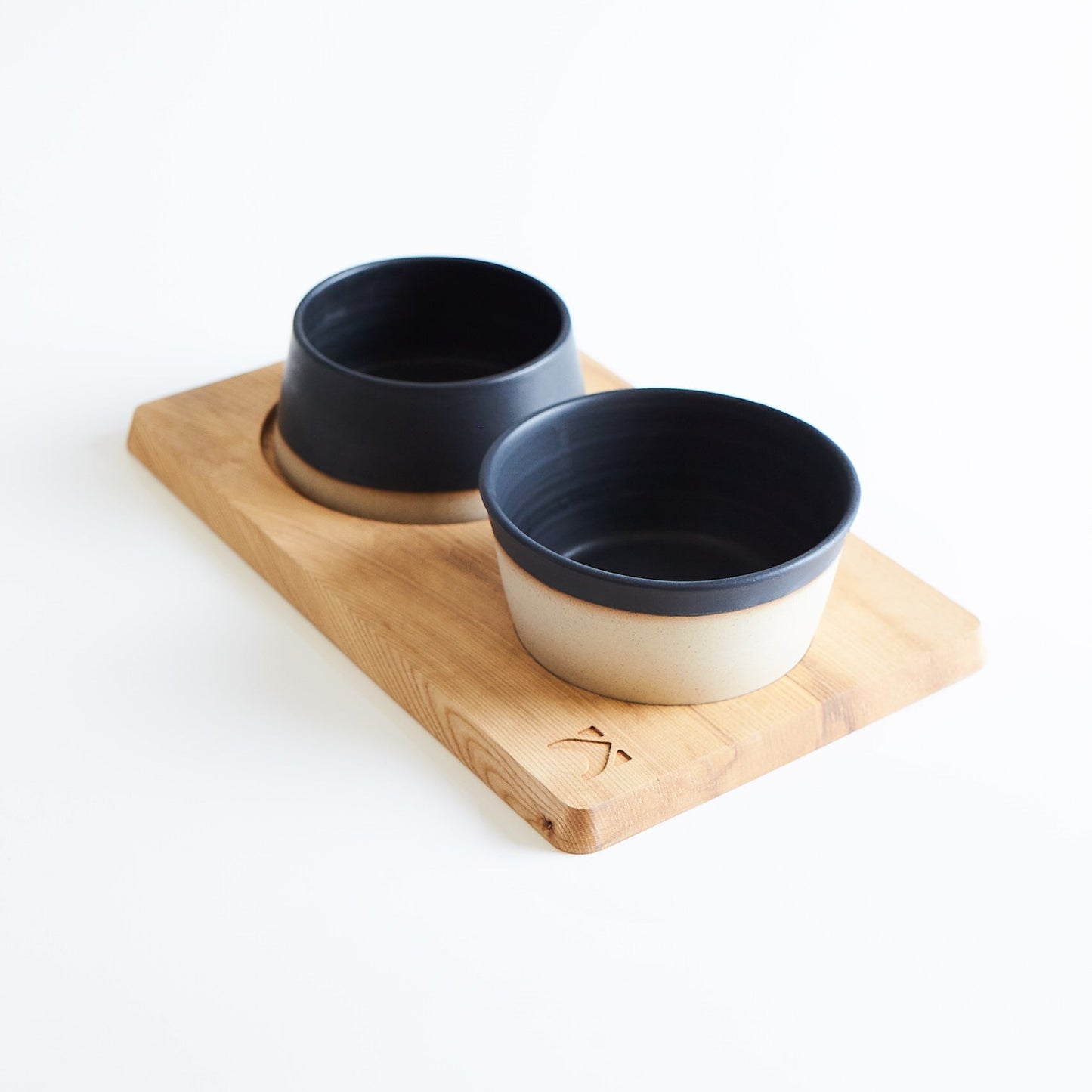 Two black ceramic bowls on a wooden tray against a white background