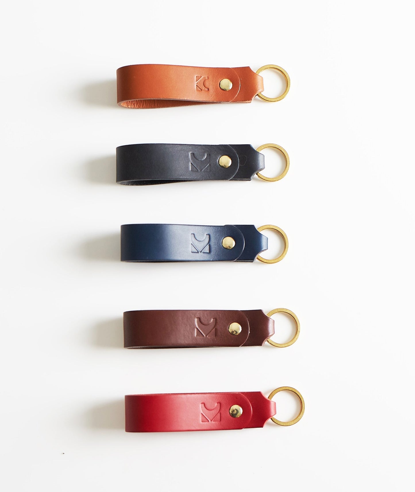 Five leather keyrings in different colors arranged vertically on a white background.