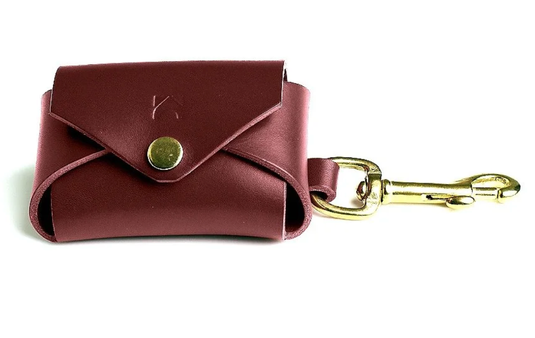 Oxblood leather poop bag holder with solid brass eyelet dispenser and clip on a white background